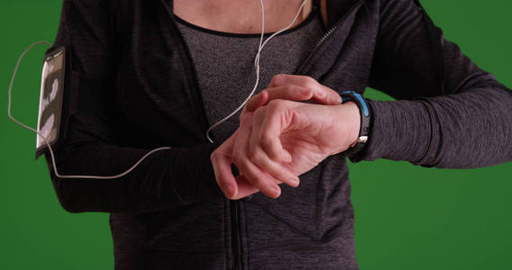女子慢跑者检查手表在运动服装在绿色屏幕上的特写镜头