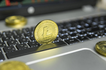 金色的 Litecoin 硬币, 用金币躺在银色笔记本电脑的黑色键盘上, 在屏幕上绘制图表图作为背景。litecoins 在线业