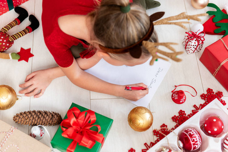 可爱的女孩写信给圣诞老人在客厅的地板上。一个年轻女孩写圣诞愿望清单的俯视