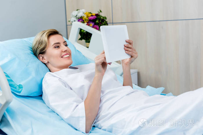 在医院病房床上使用数字片剂的微笑成年女性患者