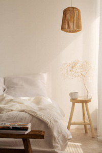 床头柜与杯子和花旁边的床与白色的床上用品, 枕头和毯子, 真实的照片与复制空间在空的墙壁上