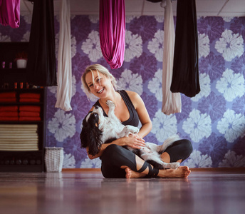 有吸引力的女人玩她可爱的狗, 而坐在地板上瑜伽健身俱乐部