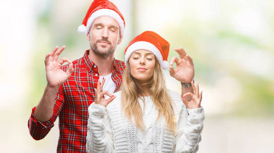 年轻夫妇在爱戴着圣诞节帽子在孤立的背景放松和微笑与眼睛关闭做冥想手势与手指。瑜伽概念