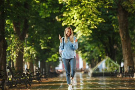 微笑的年轻女孩与背包拿着手机, 在公园散步