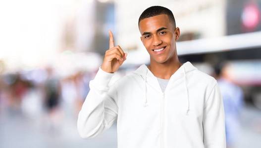 黑皮肤的年轻人, 穿着白色运动衫, 露出和举起一根手指, 表示在户外是最好的