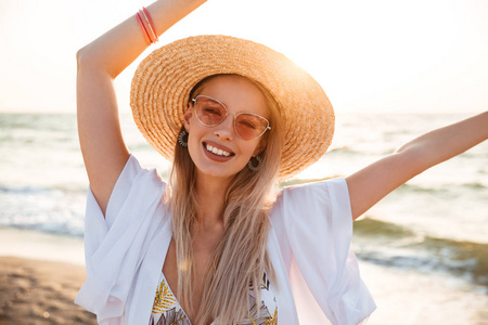 美丽的金发女人的形象20s 夏季草帽和太阳镜在海边休息时微笑