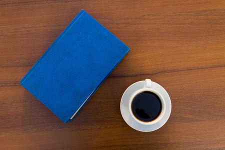 一杯咖啡和一本关在木桌上的书。顶部视图