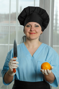 女厨师手里拿着一个橘子, 另一只手拿着一把小刀。