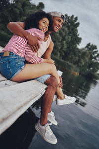 微笑的情侣在爱拥抱和坐在码头在湖