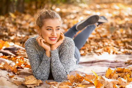美丽的年轻妇女说谎在格子与干燥的叶子在秋天公园