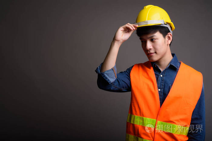 年轻英俊的亚洲人建筑工人反对灰色的背水一战
