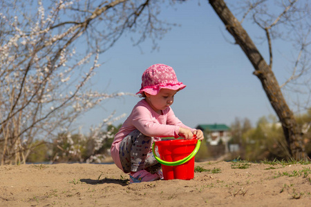 可爱的小女孩在沙子里玩红色的水桶