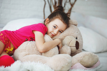 一个年轻的长发女孩穿着粉红色的 t恤衫, 短裤和高尔夫的谎言, 抱着玩具熊在床上的垫子和树枝