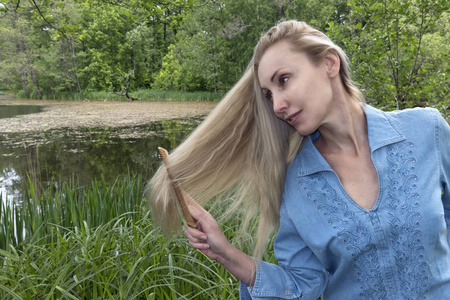 美丽的女人在夏天天梳长长的头发在河岸边