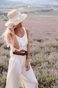 时尚的户外照片美丽的感性女孩与金发在优雅的白色礼服和秸秆配件摆在普罗旺斯薰衣草领域