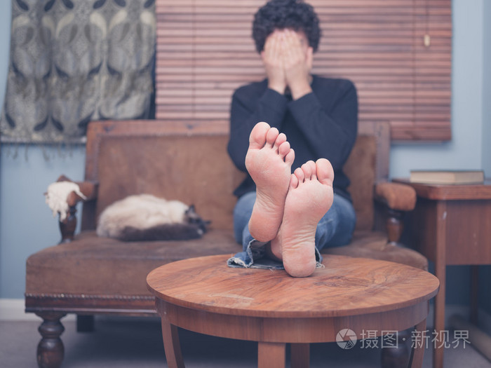 赤脚男人坐在沙发上,遮住他的脸