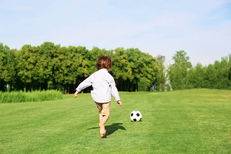 可爱的小男孩在公园踢足球在晴朗的天