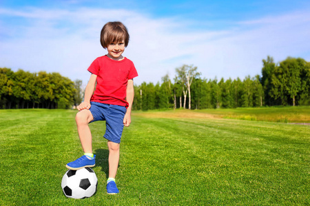 可爱的小男孩与足球在公园在晴朗的天