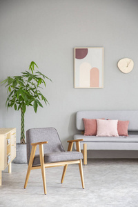 木扶手椅在粉红色和灰色客厅内与海报以上沙发上的枕头。真实照片