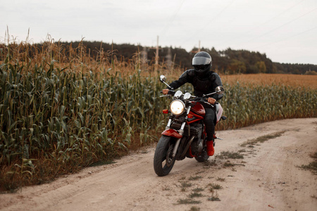 男子是一个骑摩托车的黑色装备与头盔骑马在田里与玉米。概念旅行