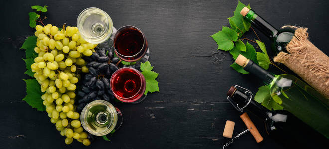 在瓶子和玻璃杯中设置红酒和白酒。葡萄。在黑色的木质背景。文本的可用空间。顶部视图