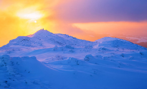 日出照亮天空，山和树站在雪堆被冻雪与黄色光芒覆盖