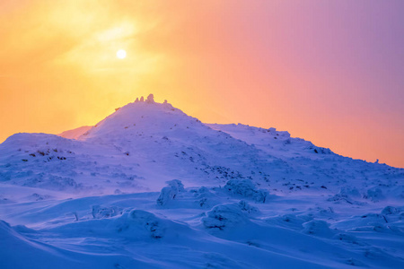 日出照亮天空，山和树站在雪堆被冻雪与黄色光芒覆盖