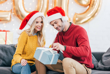 年轻夫妇在圣诞老人帽子与圣诞节礼物在家与2019金黄气球