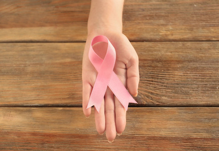 在木质背景上持有粉红色丝带的妇女。乳癌意识概念