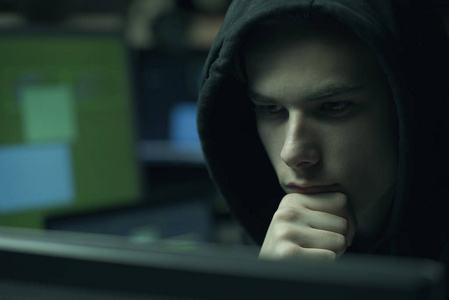 酷年轻的黑客与帽衫工作的计算机, 网络犯罪和数据安全概念