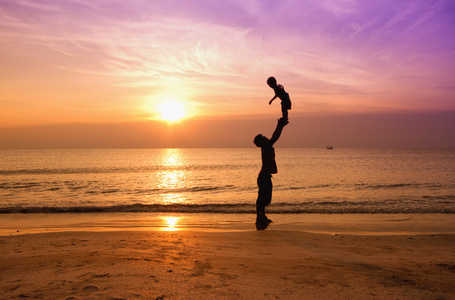父亲和儿子在日落海滩上的剪影