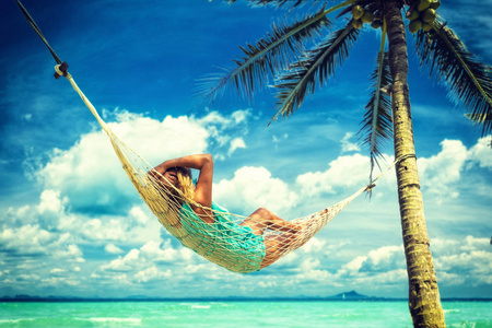 坐在沙滩上的吊床上的女人。旅游度假理念