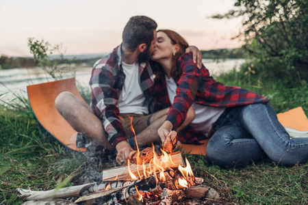 快乐的年轻夫妇坐在篝火上的自然野餐