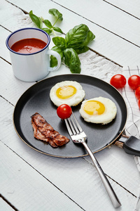 两个美味的煎鸡蛋和煎培根在一个白色的厨房桌子上, 西红柿汁和罗勒叶