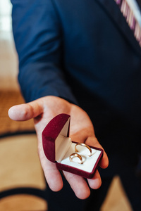 新郎持有黄金结婚戒指饰品礼品盒。男子在西装和领带拿着订婚戒指
