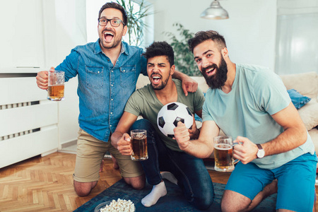 快乐的男性朋友看电视上的运动和喝啤酒