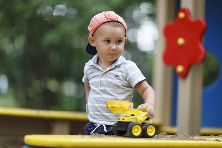 严重男孩玩玩具车在沙箱在院子里夏天