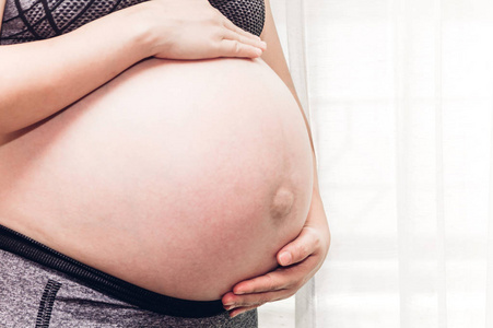 怀孕的妇女纵向触摸她的肚子在窗口附近的家