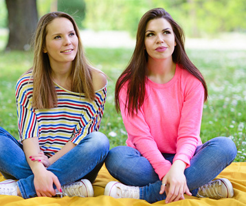 在夏季的一天坐在草地上的两个年轻女孩朋友