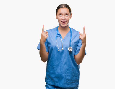 年轻的白种人医生妇女穿医疗制服在孤立的背景惊讶和惊讶地看着手指和举起的胳膊