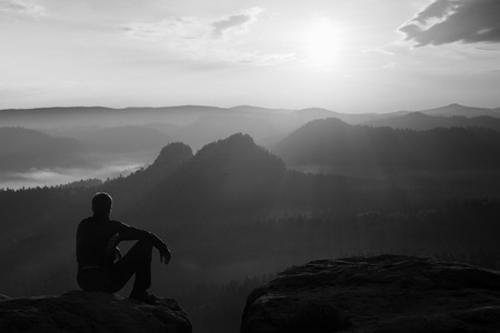 在黑色的风夹克坐上锋利的岩石和观看到多彩迷雾笼罩的山谷贝娄的旅游。阳光明媚的春天黎明在洛矶山脉