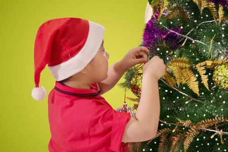 在装饰圣诞树时戴着圣诞老人帽子的可爱小男孩的背面视图