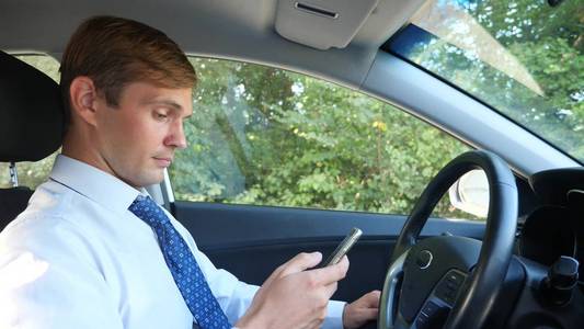 穿着衬衣和领带的男商人正在开车, 在手机上浏览信息。违反交通规则