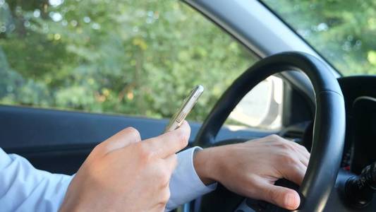 手和方向盘的特写。一个男商人正在开车, 在他的手机上浏览信息。违反交通规则