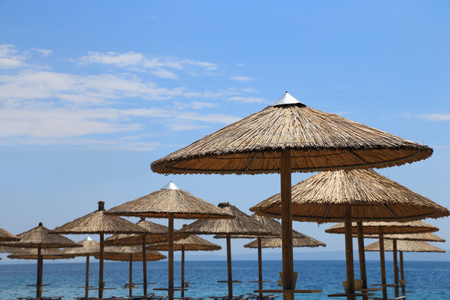 阳光明媚的海滩与柳条遮阳伞和蓝蓝的天空