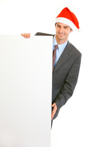 高兴的是年轻的商人在圣诞老人帽子持有空白广告牌