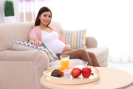 托盘与美味的早餐和背景上的美丽怀孕的女人