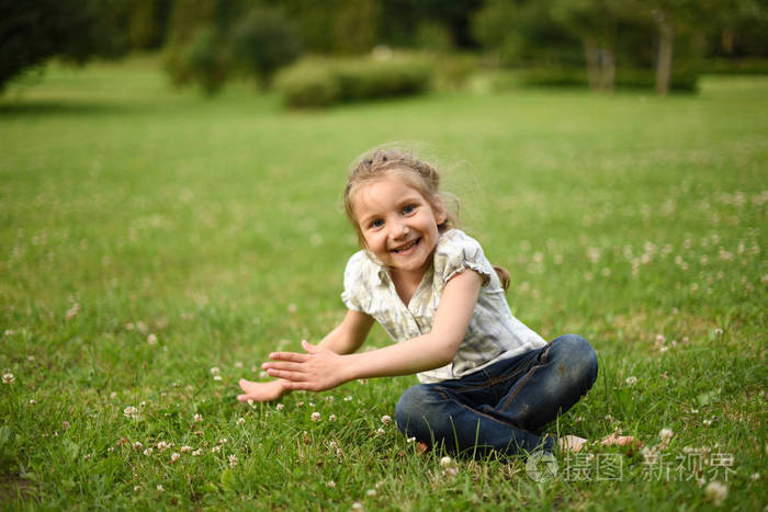 笑着坐在明亮的绿色草地上的小女孩