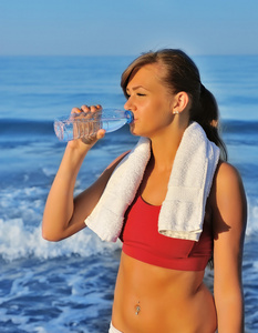 美丽的女孩饮用水上海滩运动后