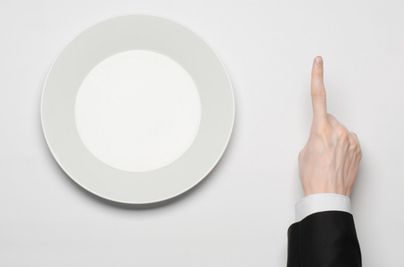 商务午餐和健康食品主题 男人的手在一套黑色的西装，拿着一个白色的空盘子和孤立的白色背景上显示手指手势，在工作室顶视图